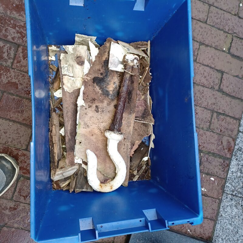 Restanten van een afgekeurde houten hijsbalk met verroeste hijshaak in een krat